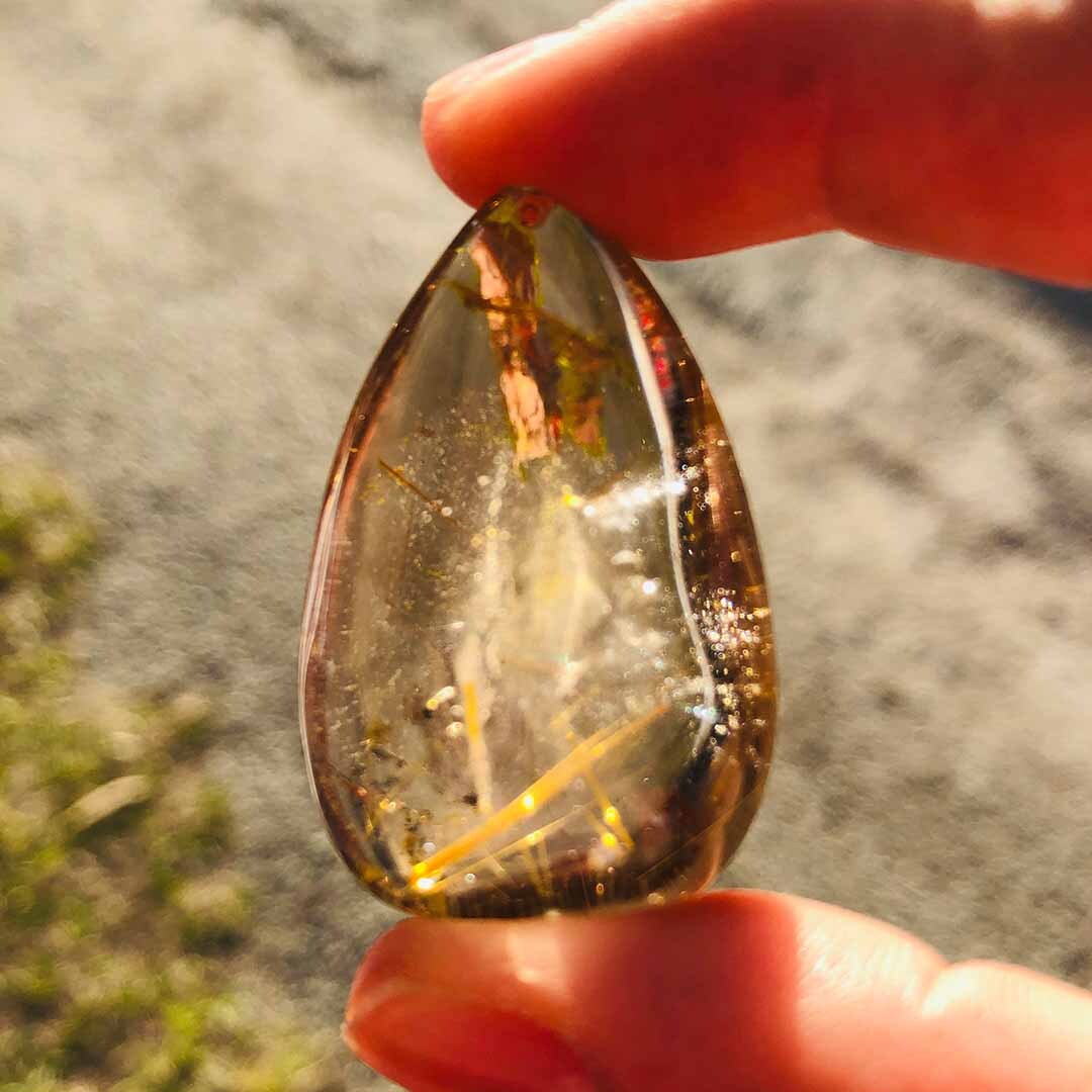 Rutilated Quartz Teardrop Pendant between fingers