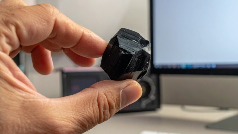 Hand holding Tourmaline near computer