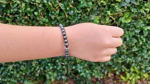 Hand wearing a Hematite 6mm bracelet Hand wearing a Hematite 6mm bracelet with green hedge behind